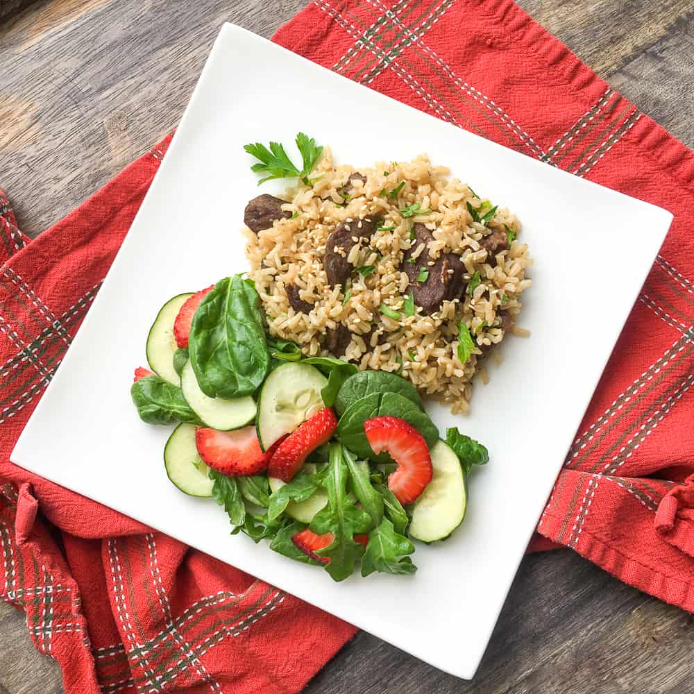 mixed greens with cucumbers and sliced strawberries on a white plate with instant pot beef and rice dish