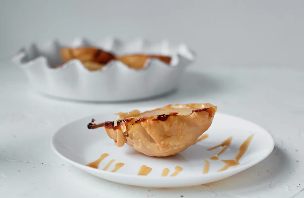 side view of pear tart on a white place with caramel sauce drizzled on it