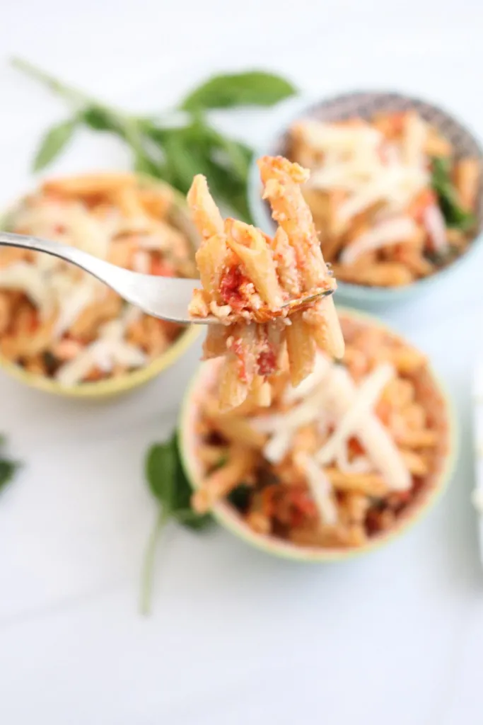 instant pot feta pasta tiktok on a fork with 3 dishes behind it