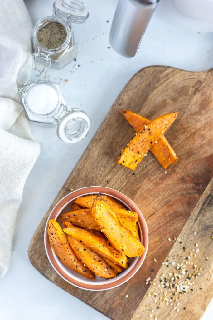air fryer sweet potato wedges on a wooden cutting board in a small white bowl