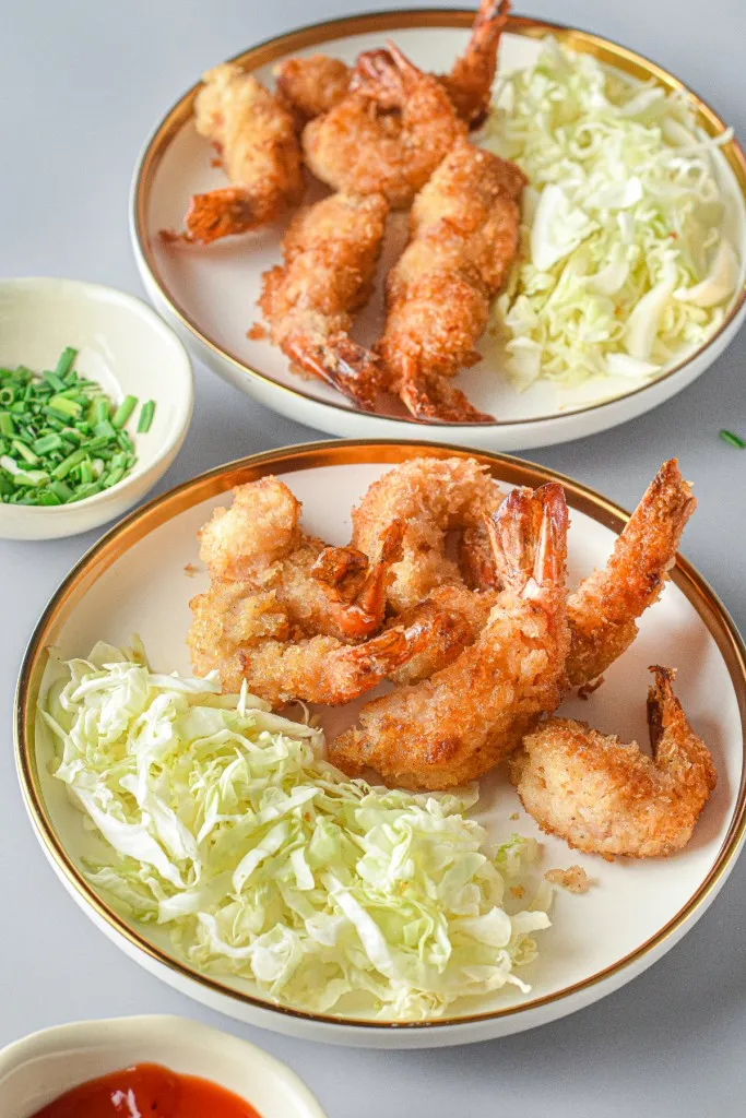 2 plates of panko fried shirmp with tails on and little beds of shredded lettuce