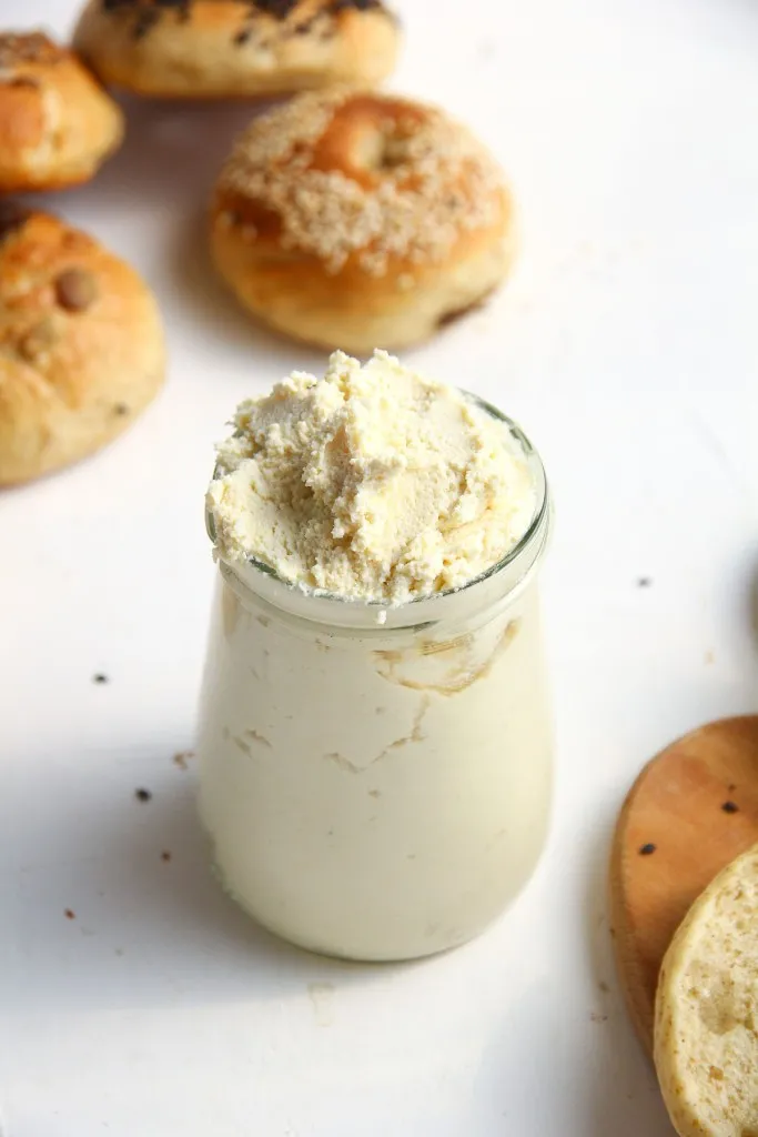 a glass jar full of homemade vegan cream cheese with bagels