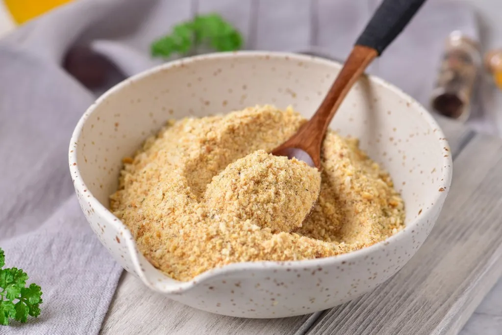 A wooden spoon with homemade breadcrumbs in a white bowl with brown specks