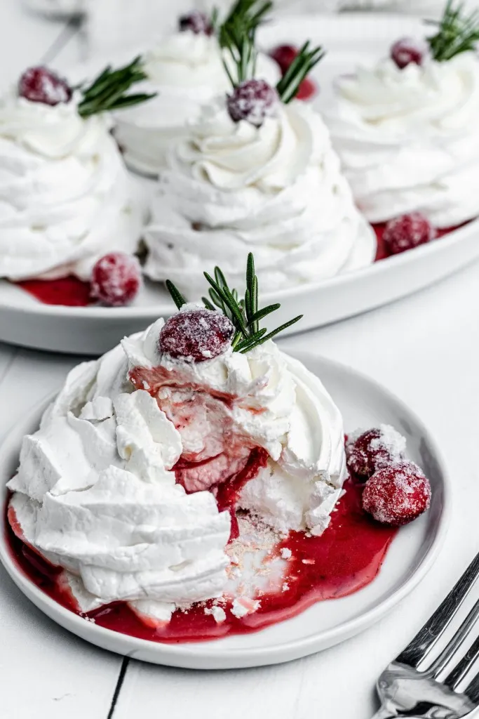 close up view of christmas pavlova with sugared cranberries and rosemary sprig