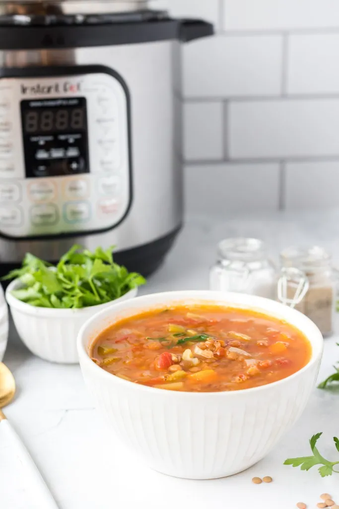 a bowl of fresh made lentil soup in a white bowl next a bowl fresh parsley