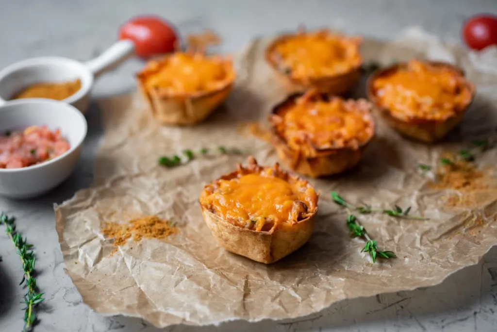close up view mini mexican pizzas on parchment paper with a bowl of salsa with red peppers and tomatoes in background