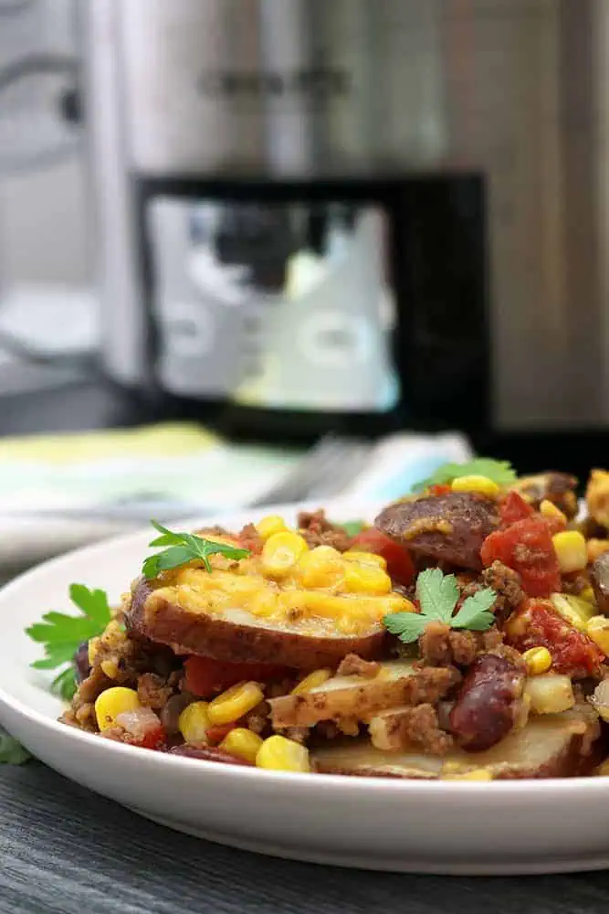 cowboy potatoes on a white plate in front of a black and silver crockpot