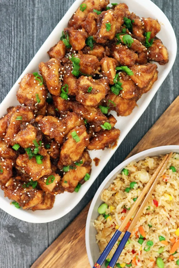 vegetable fried rice and slow cooker general tso's chicken on a white plate and dark grey table