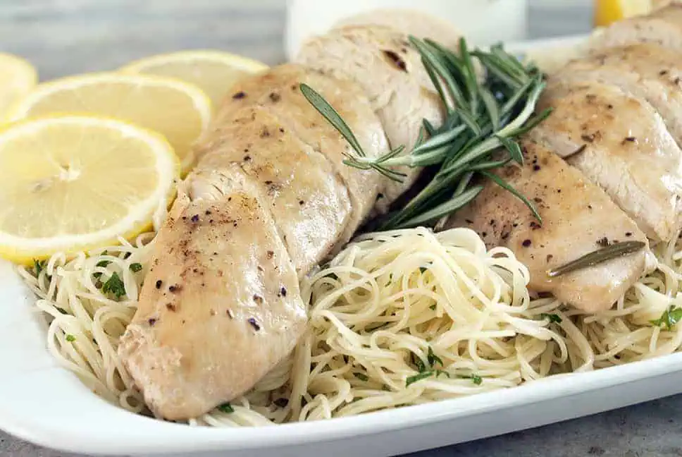 side view of rosemary slow cooker lemon chicken over angel hair pasta with fresh lemons