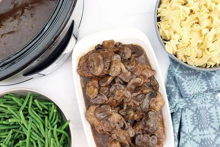 slow cooker salisbury steaks on a white plate with a blue napkin next to a crockpot