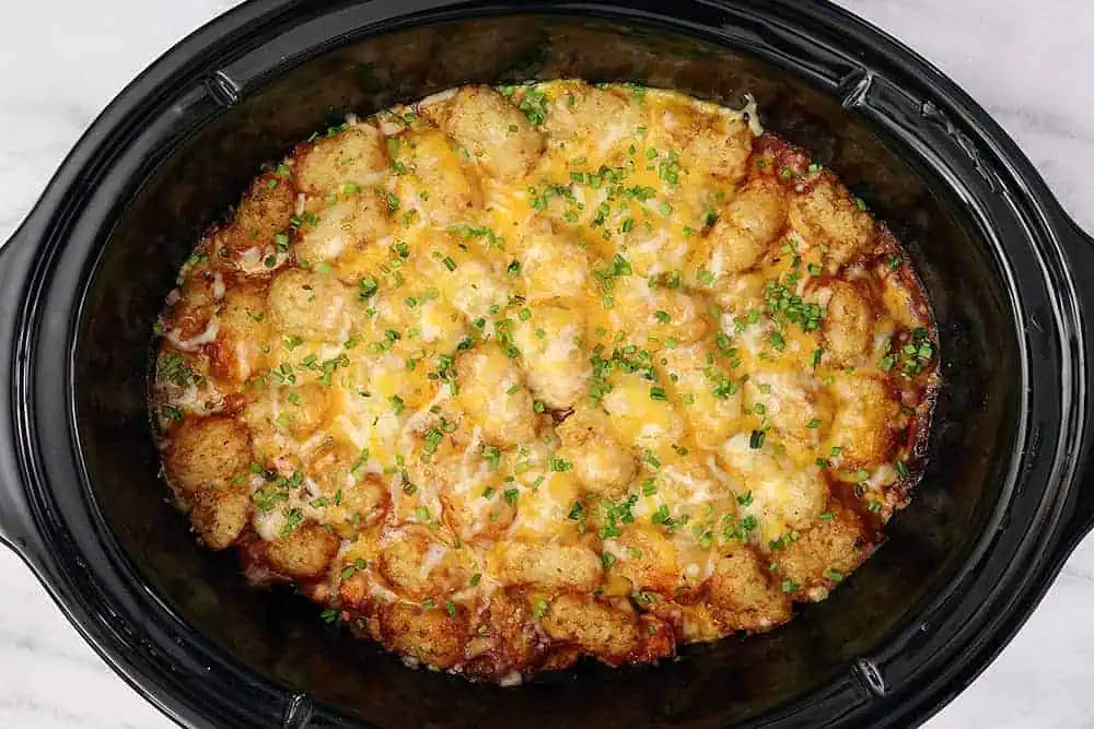 black crockpot full of tater tot casserole and garnished with diced chives