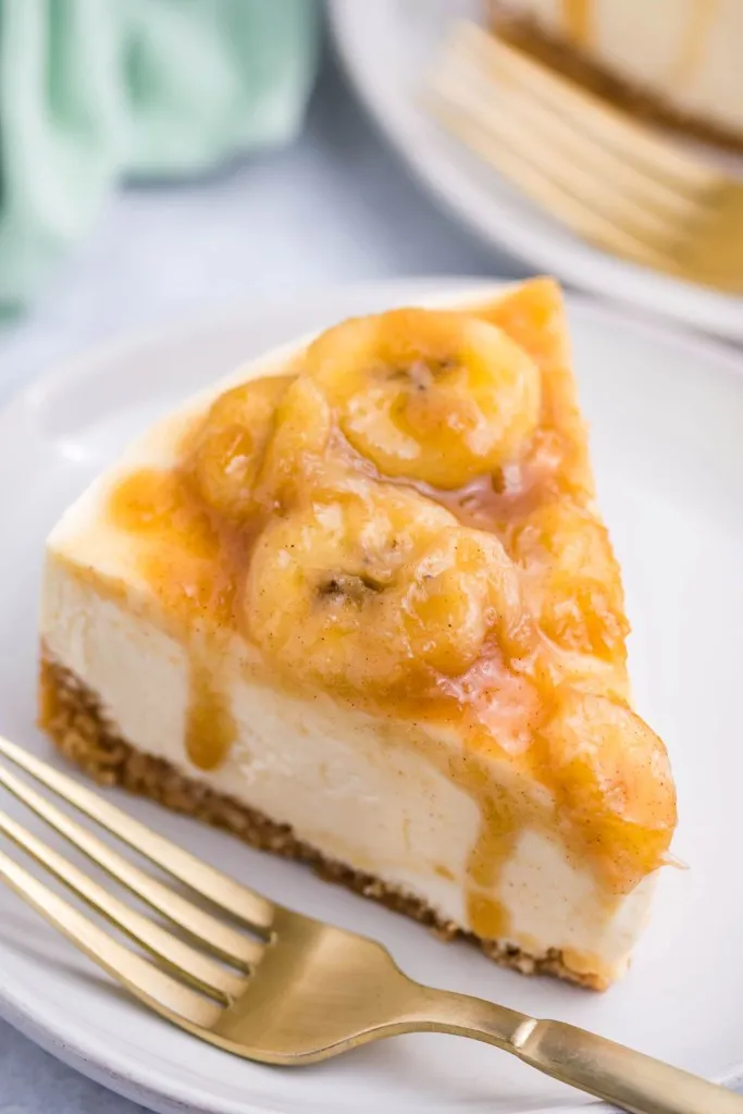 close up shot of instant pot bananas foster cheesecake on a white plate and gold fork
