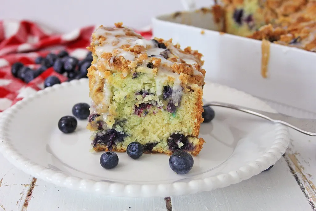 glaze drizzled blueberry coffee cakes with a streusel crumb topping with a red and white checkered napkin