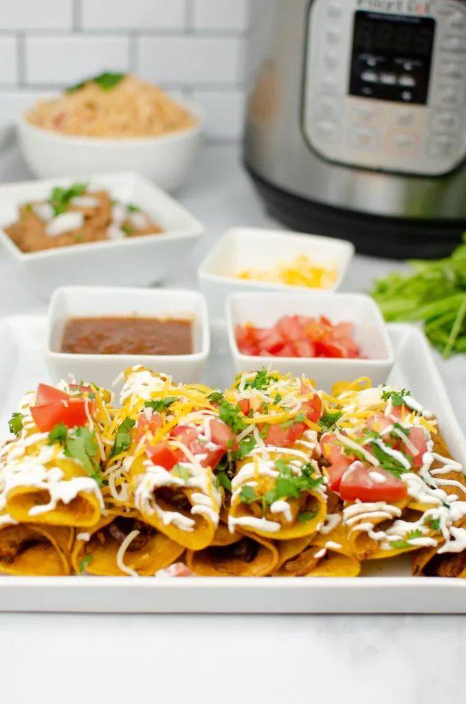 instant pot chicken taquitos garnished with diced tomatoes and cilantro