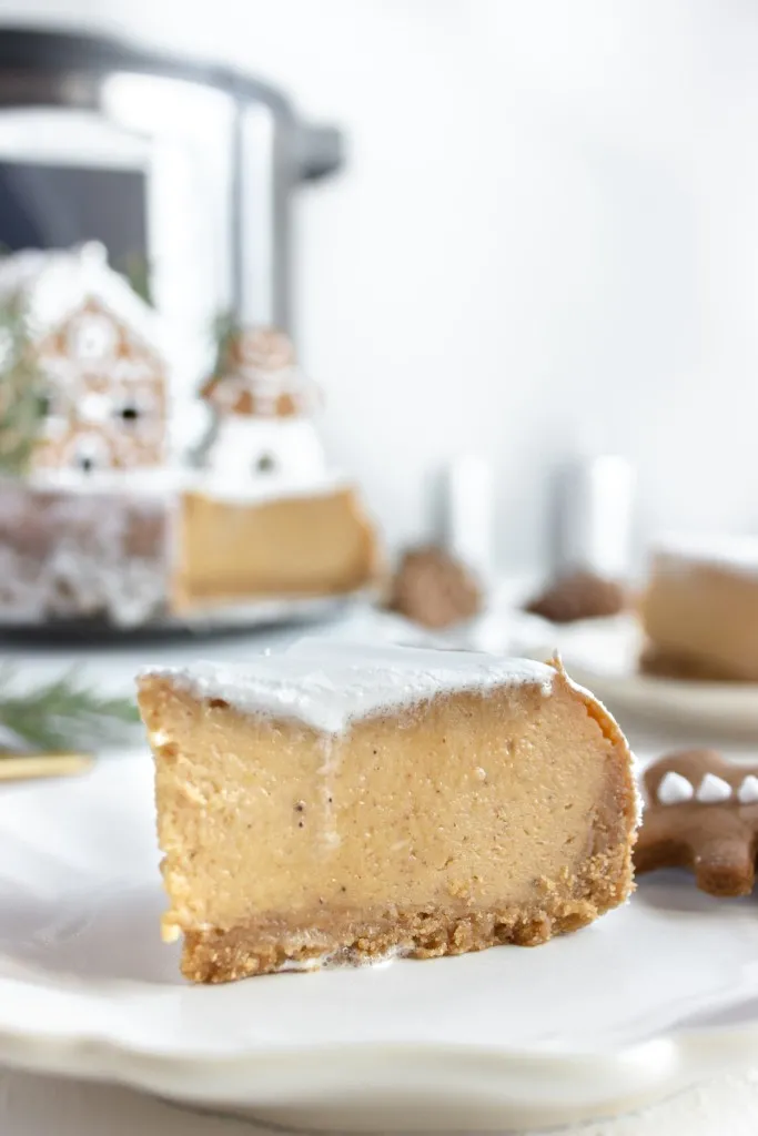 sideview instant pot gingerbread cheesecake and whipped cream on top on a white plate and cookies in the background