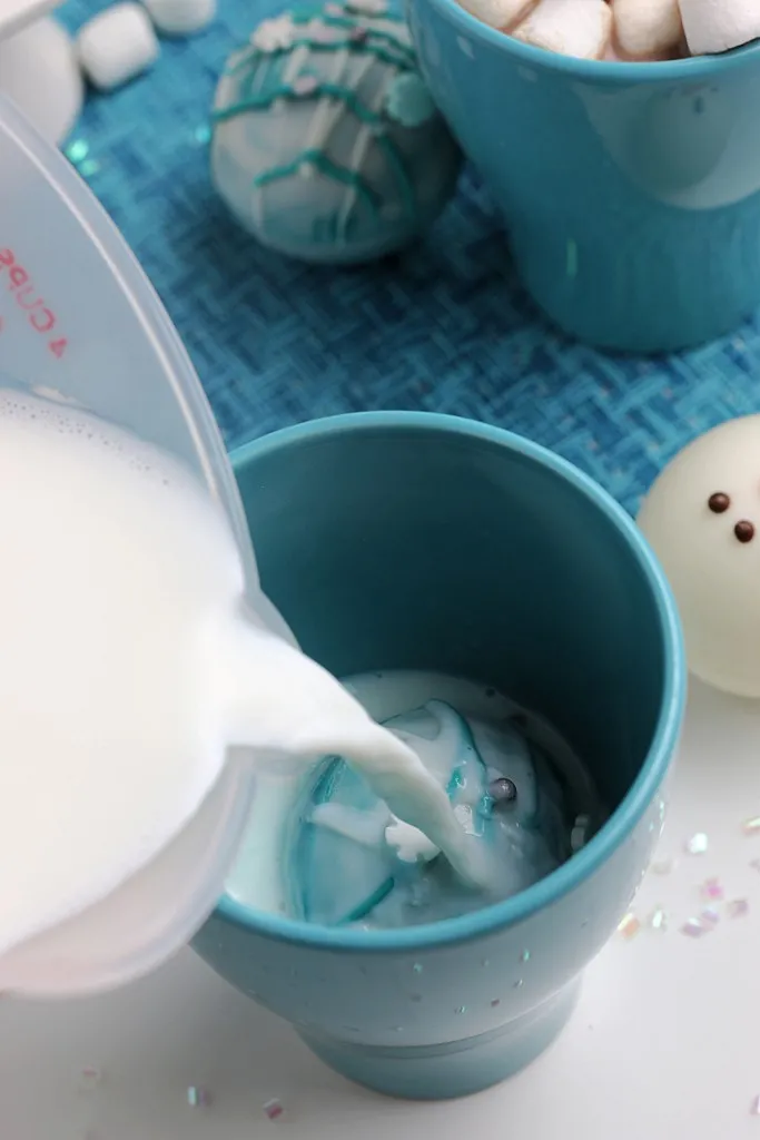 hot milk being poured over a hot cocoa bomb