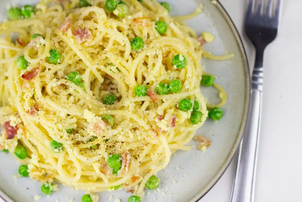 close up view of fresh made recipe of pasta carbonara with viewed pieces of pancetta and peas