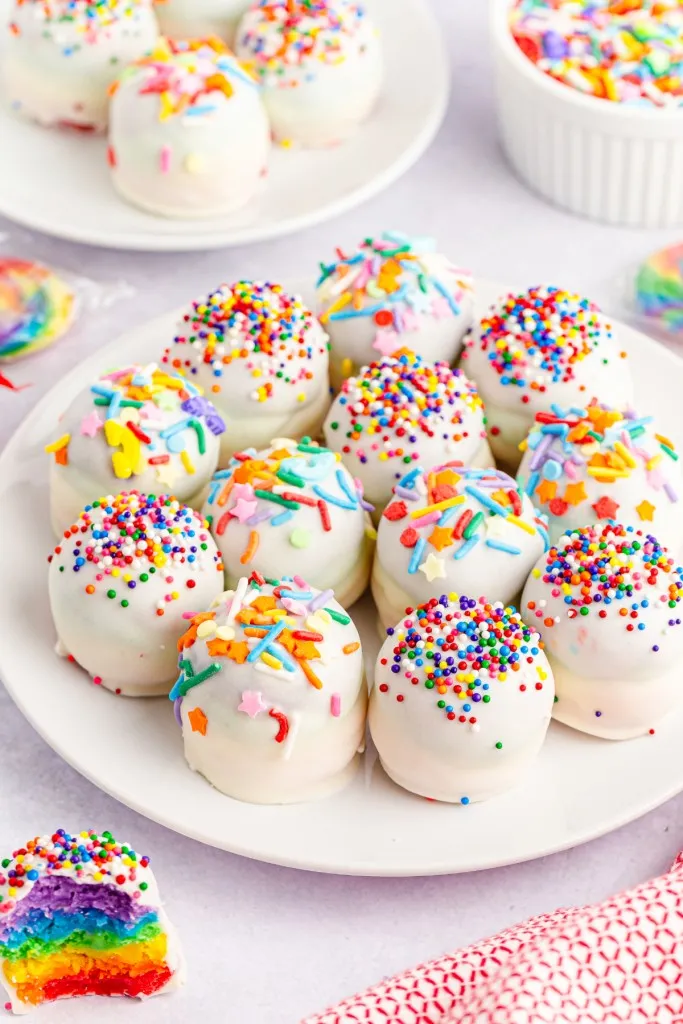rainbow cake balls with colorful sprinkles on a white round plate
