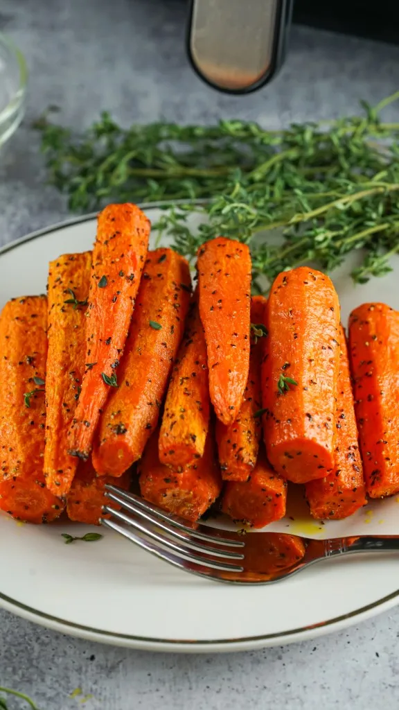 overhead shot of a pile of herb roasted air fryer carrots and a gold trimmed white platter with fresh herbs