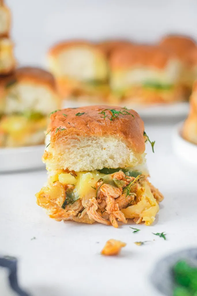 a single slider in front of a plate full of chicken sliders flavored with a delicious buffalo sauce and other seasonings
