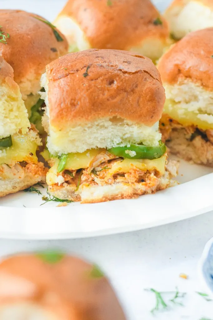 The best chicken sliders on a white plate with fresh slices of jalapenos