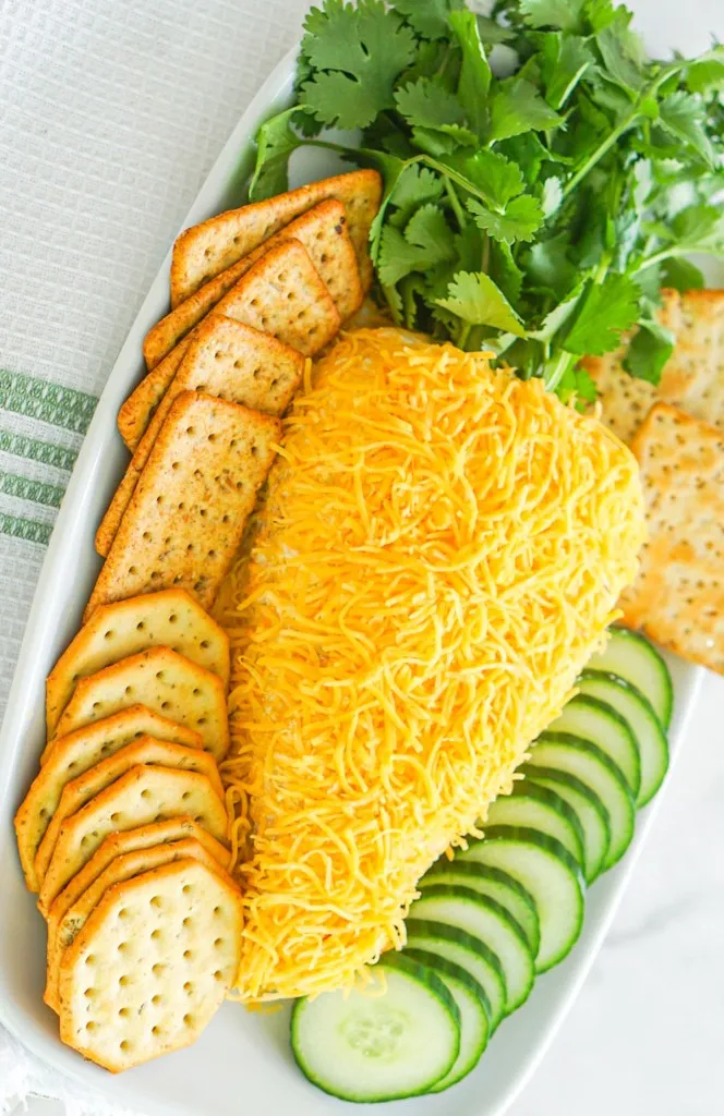 carrot cheese ball with parsley as the top on a white rectangle plate