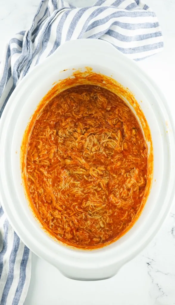 a white ceramic crockpot full of buffalo chicken