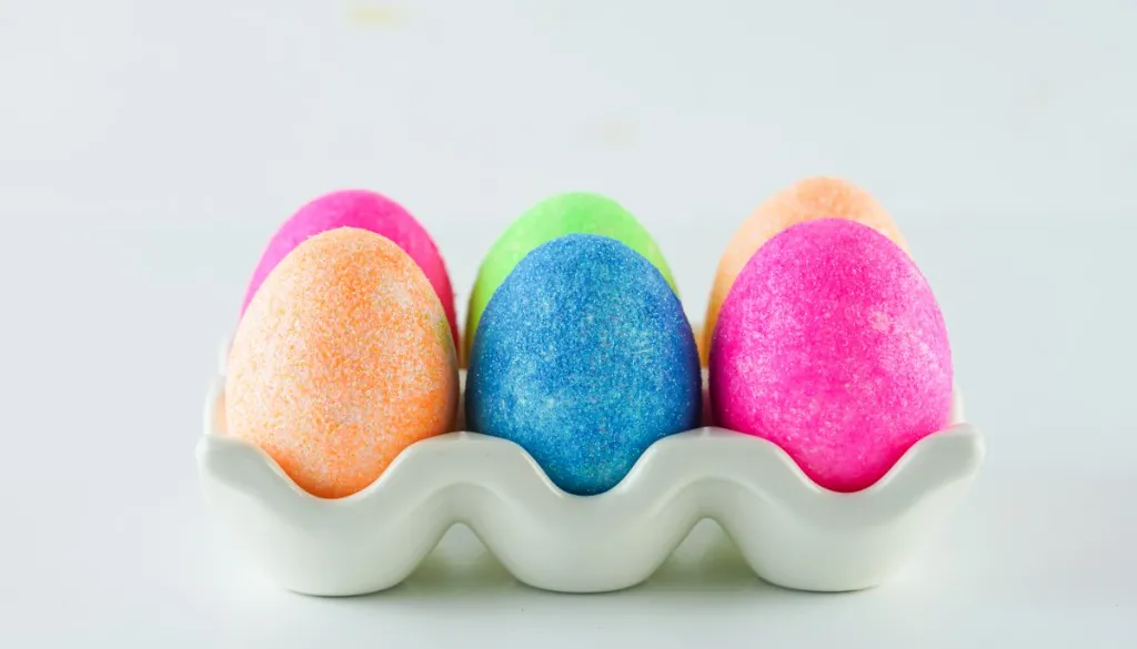 beautiful multicolored glitter easter eggs in a white ceramic egg carton