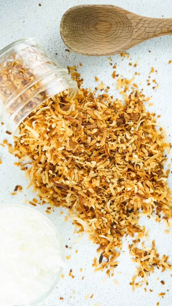 overhead shot of toasted coconut in a class jar on a marble background