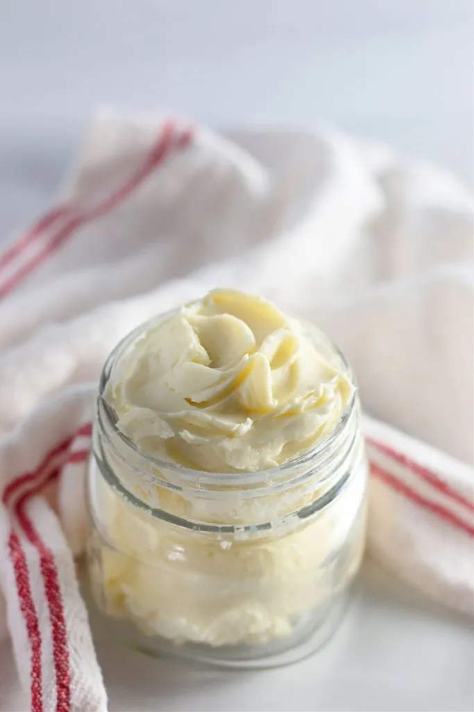 Glass jar of fresh butter with a white a red striped kitchen cloth on a white marble countertop.