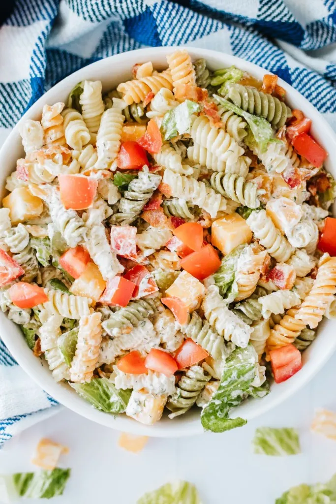 Overhead view of a bowl of BLT Pasta Salad on a white kitchen countertop with a blue and white checkered cloth.