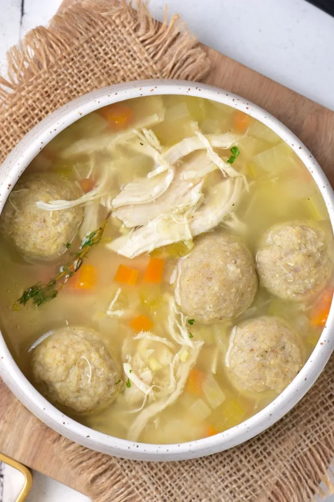 Close up of a bowl of Matzo ball soup on a wooden kitchen board.
