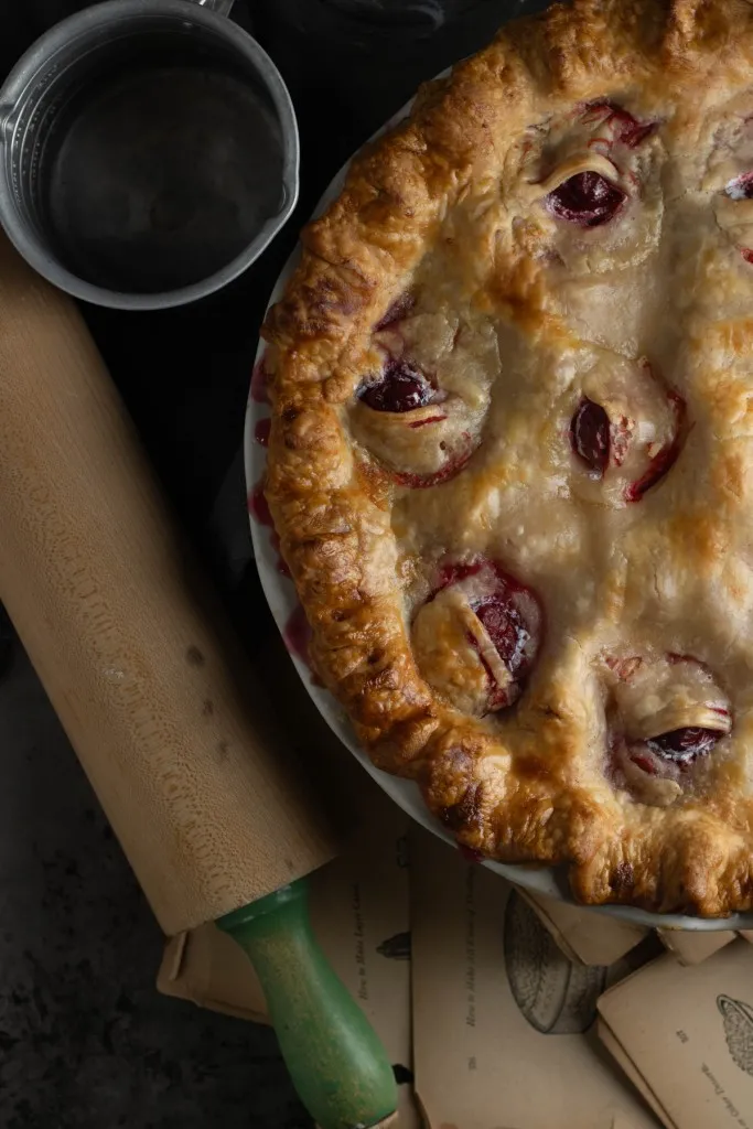Overhead view of half of an cherry rhubarb eyeball pie, wooden rolling pin, on a Halloween-themed countertop.