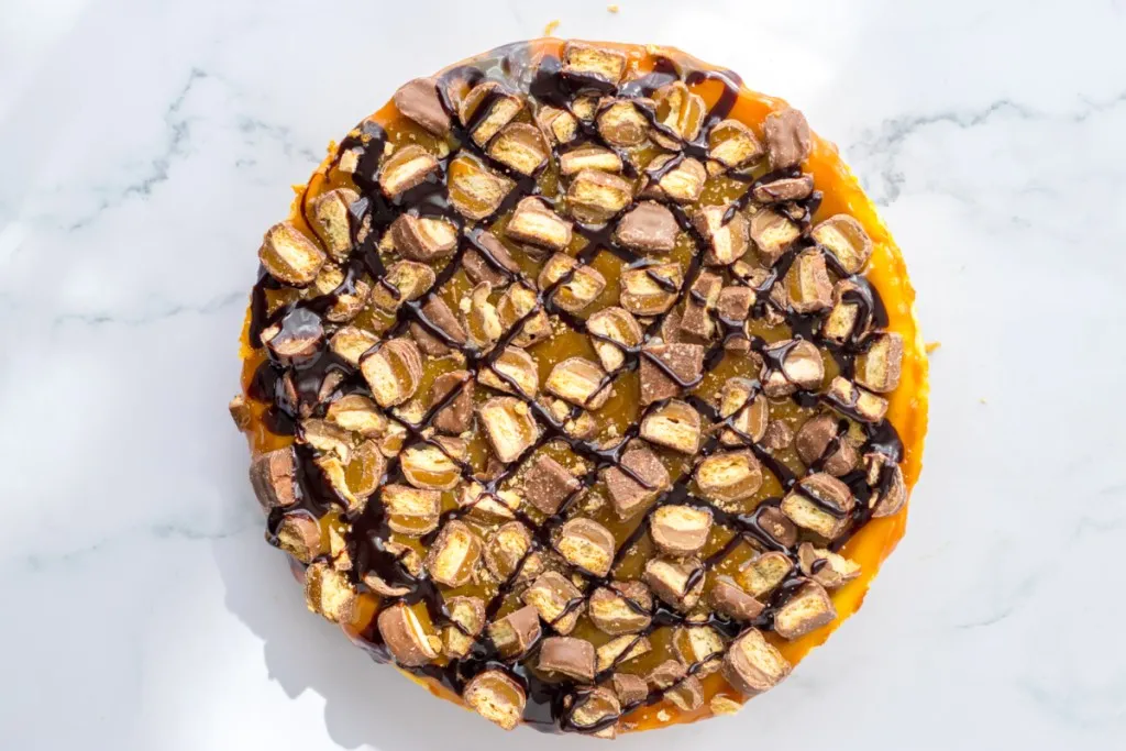 Overhead view of a Twix cheesecake on a marble countertop.