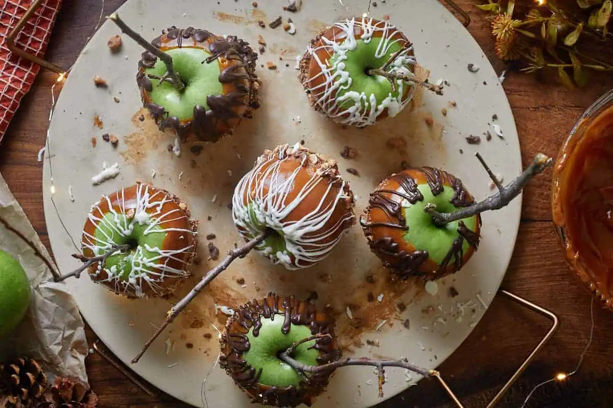 Best caramel apples coated in caramel sauce, melted chocolate, and toffee bits, on a large serving board.