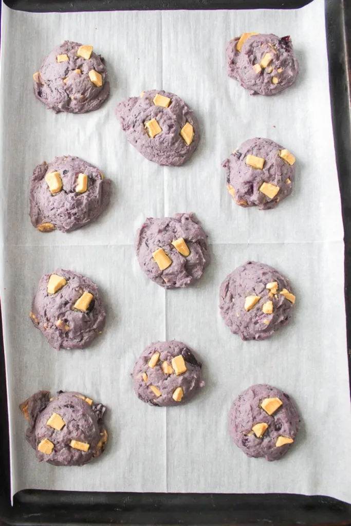 Baking tray lined with parchment paper and blueberry white chocolate cookies.