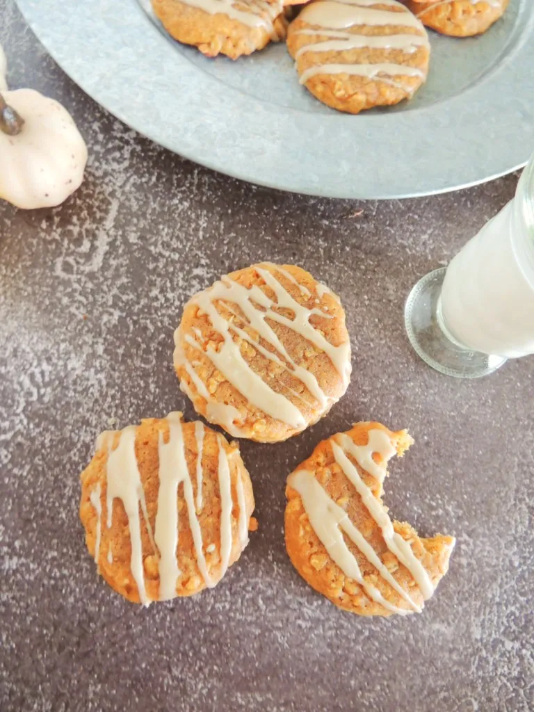 Overhead view of oatmeal pumpkin cookies, a bite taken from one of the cookies, glass of milk.