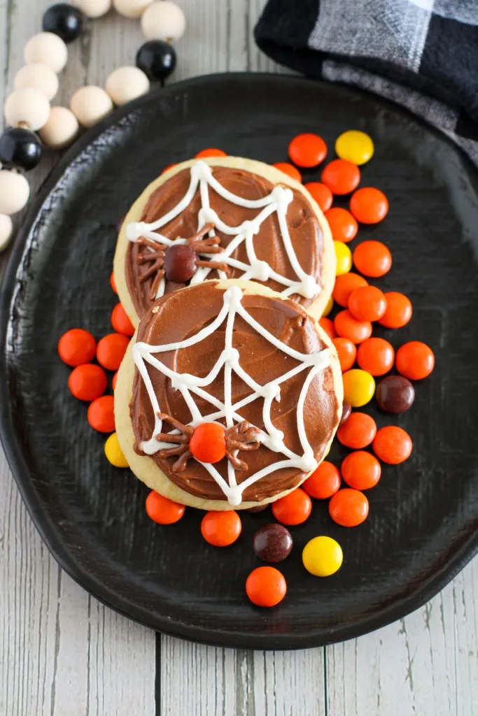 Easy spider web sugar cookies on a black plate with Reese's pieces candy.