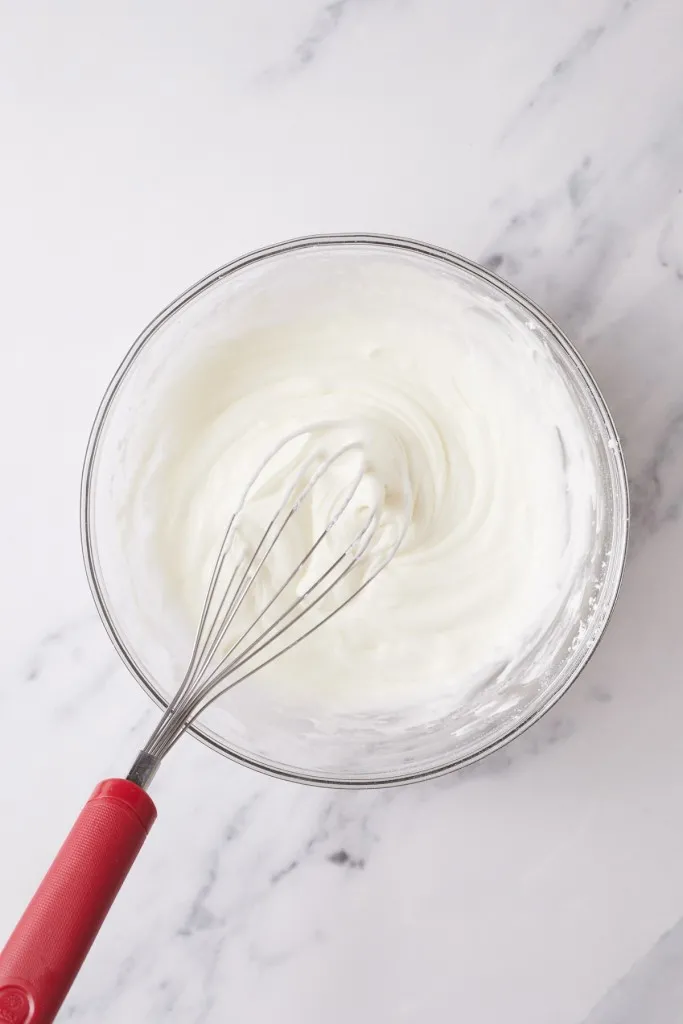 Mixing bowl with frosting and metal whisk.