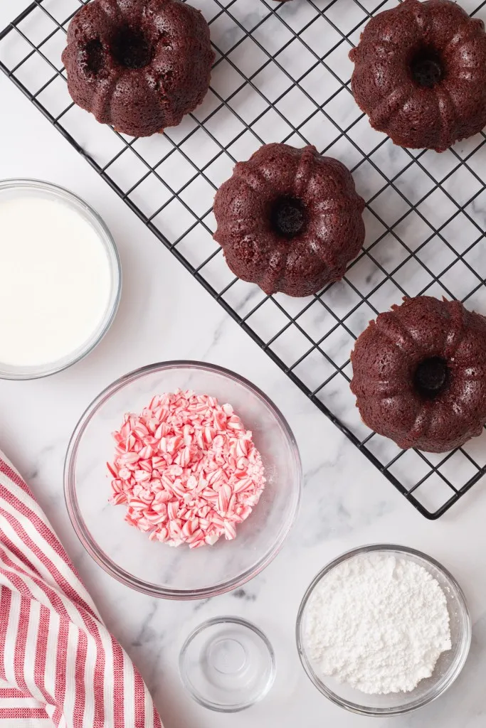 Mini chocolate bundt cakes on a wire rack, frosting ingredients in separate bowls.
