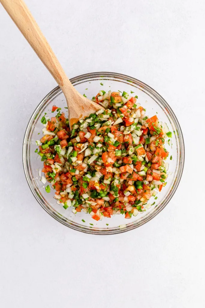 Pico de Gallo ingredients in a medium mixing bowl with a wooden spoon.