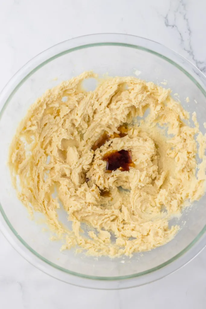 Mixing bowl with creamed butter and sugar mixture, vanilla extract, and peppermint extract.