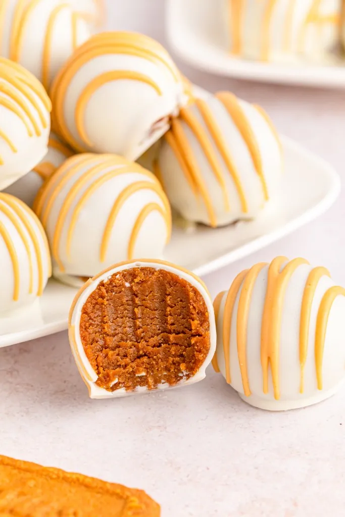 Close up of a plate piled with Biscoff truffles, front Biscoff truffle bitten in half.