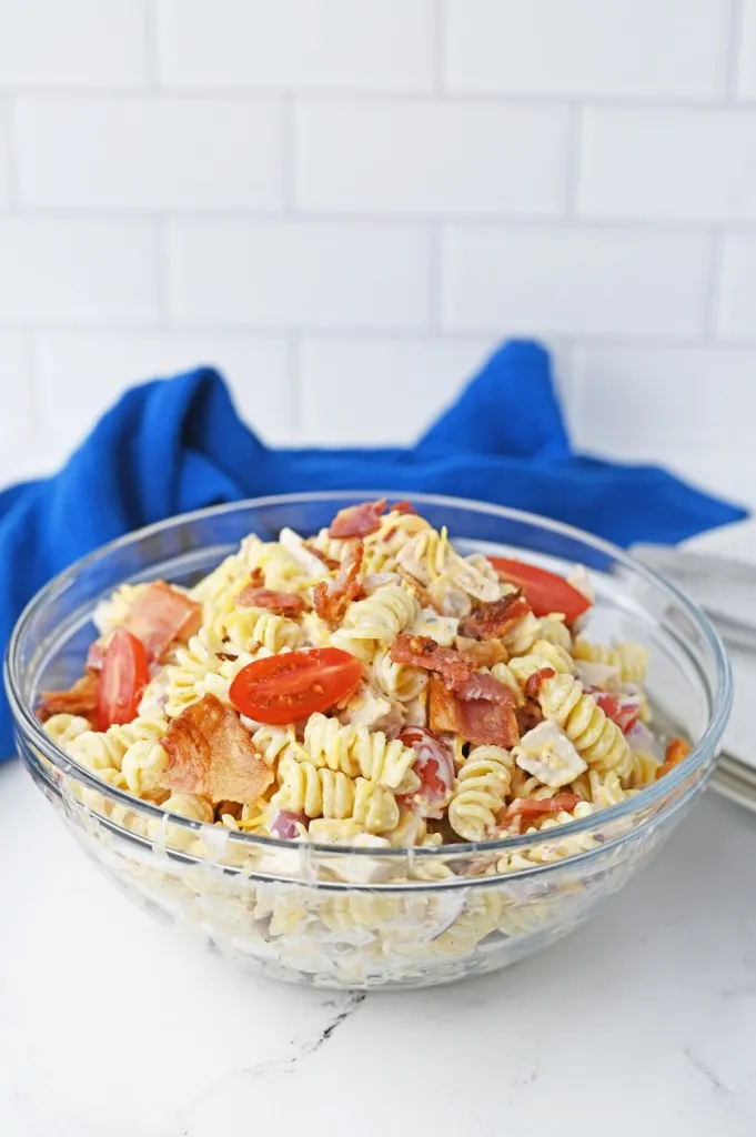 Glass serving bowl with chicken bacon ranch pasta salad, blue kitchen cloth in the background.
