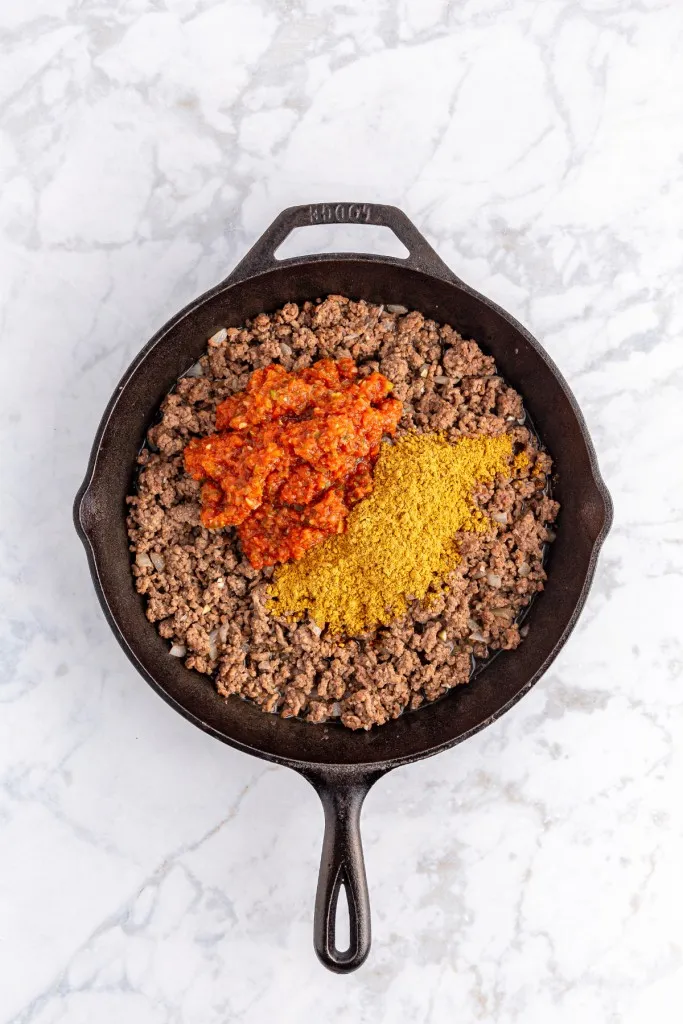 A large skillet with browned ground beef, salsa, and taco seasoning.