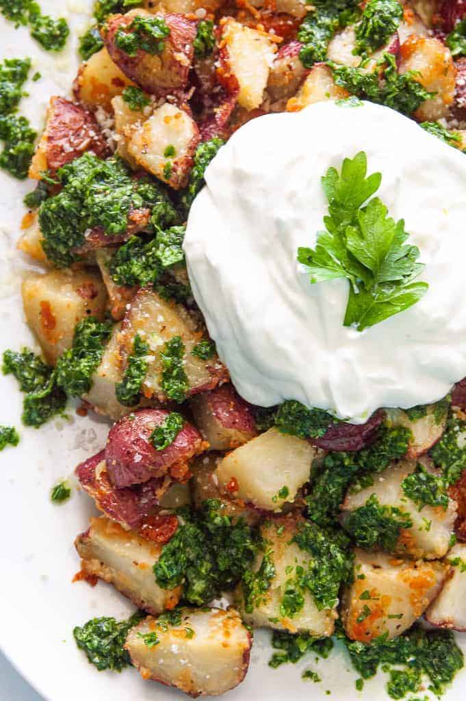 Close up of parmesan roasted potatoes with gremolata and a spoonful of Greek yogurt in the center.