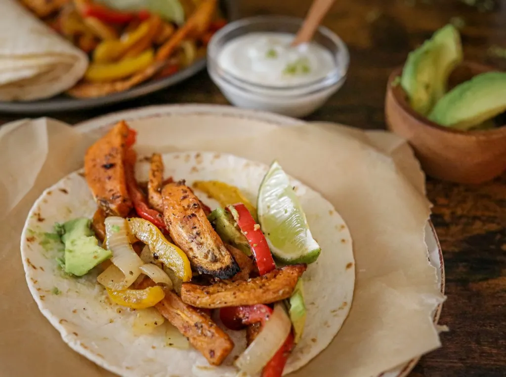 Close-up of sweet potato fajitas with avocado and zesty lime sauce in a warm tortilla.
