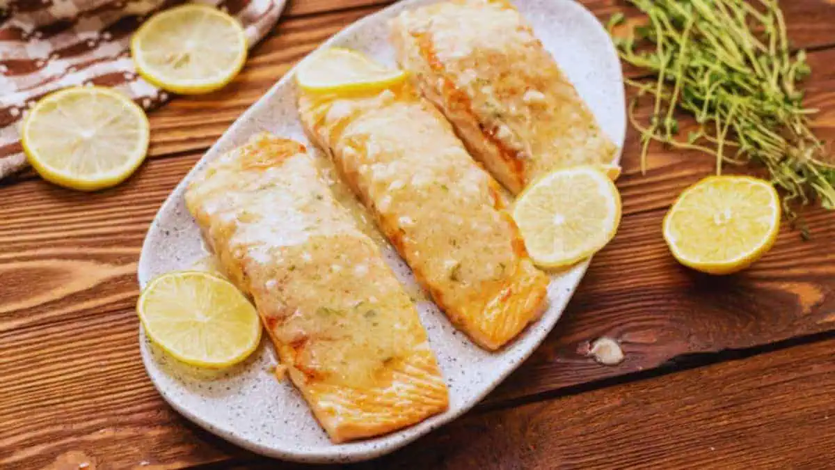 A plate with three salmon filets, covered in creamy garlic lemon sauce.