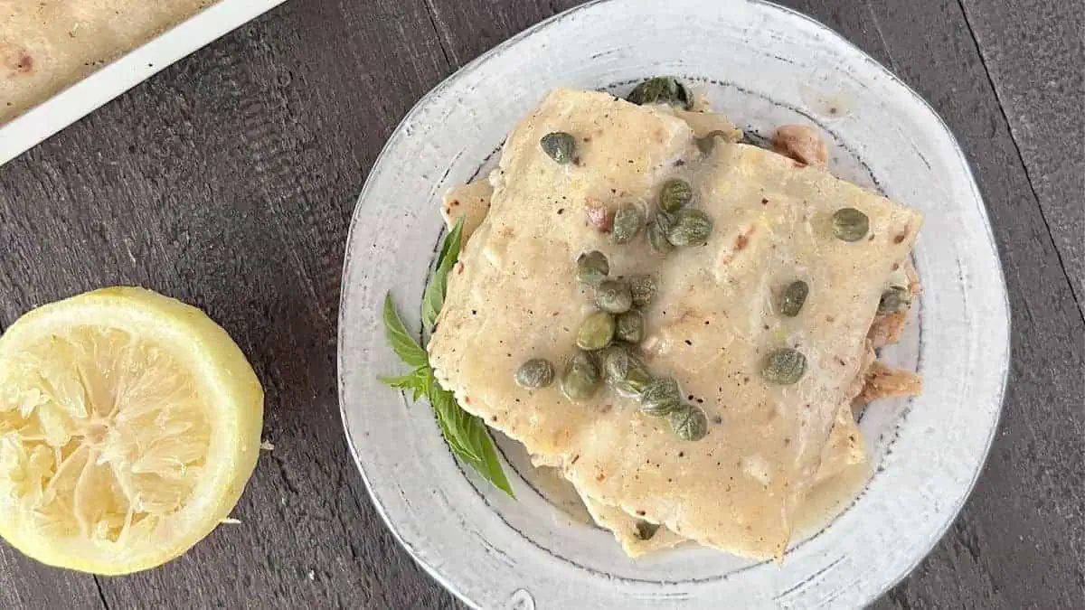 A plate of chicken lemon piccata enchiladas with capers over top.