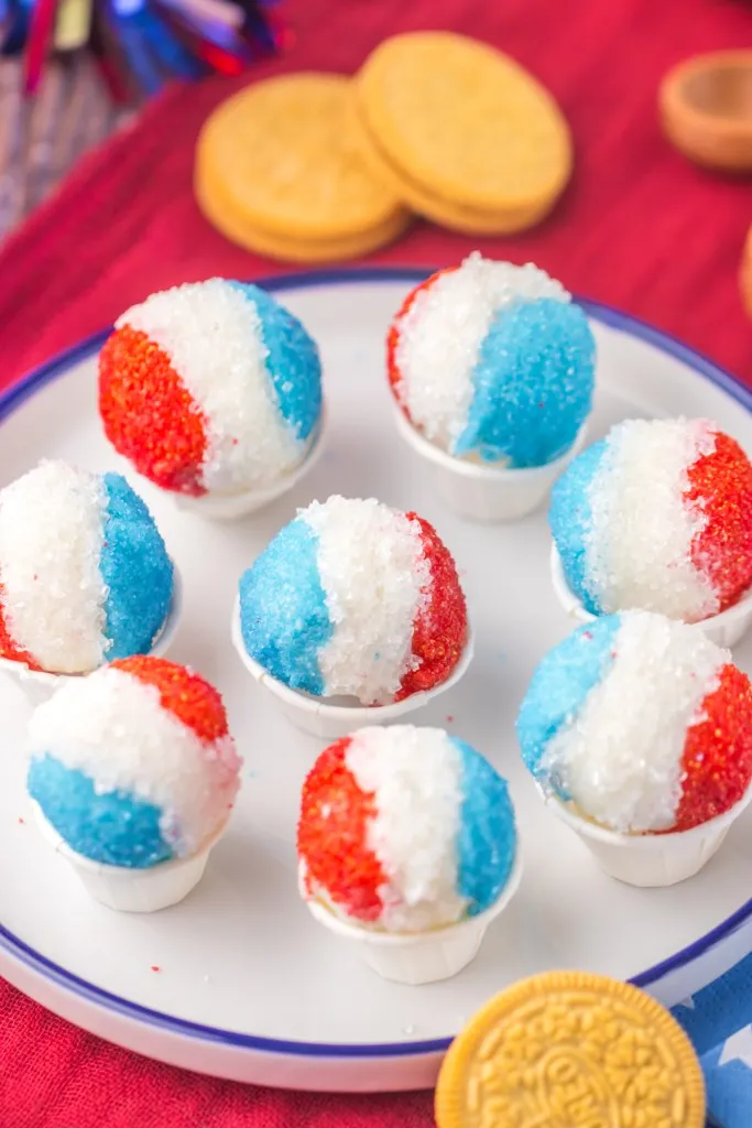 Decorated snow cone Oreo truffles sitting in little paper cups on a serving plate.